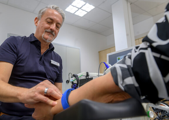 Neurologischer Facharzt bindet den Arm einer Patientin ab und hält ihre Hand fest. 